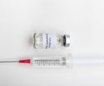 Medical vial labeled tick-borne encephalitis vaccine with a syringe on a sterile white background.