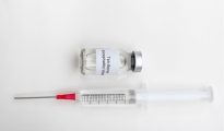 Medical vial labeled tick-borne encephalitis vaccine with a syringe on a sterile white background.