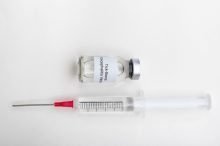 Medical vial labeled tick-borne encephalitis vaccine with a syringe on a sterile white background.