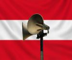 Civil defence warning siren mounted on a pole with a subtle Austrian flag background