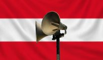 Civil defence warning siren mounted on a pole with a subtle Austrian flag background