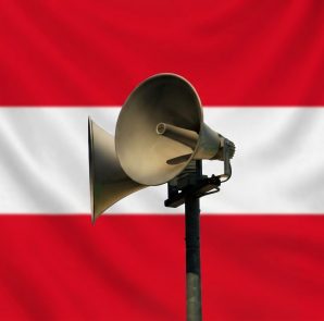 Civil defence warning siren mounted on a pole with a subtle Austrian flag background