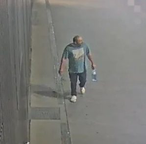 Surveillance camera footage showing the suspect walking along a sidewalk wearing a t-shirt, dark trousers, and white shoes