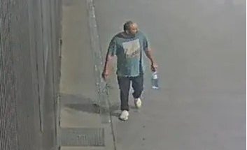 Surveillance camera footage showing the suspect walking along a sidewalk wearing a t-shirt, dark trousers, and white shoes