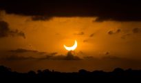 Partial solar eclipse crescent glowing near the horizon against a warm sunset sky.