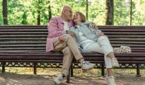 Elderly couple sitting together on a park bench in a sunny green garden