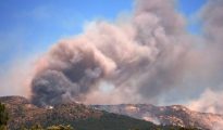 Large plume of thick smoke billows into the sky over mountainous forest terrain in Valencia, Spain.